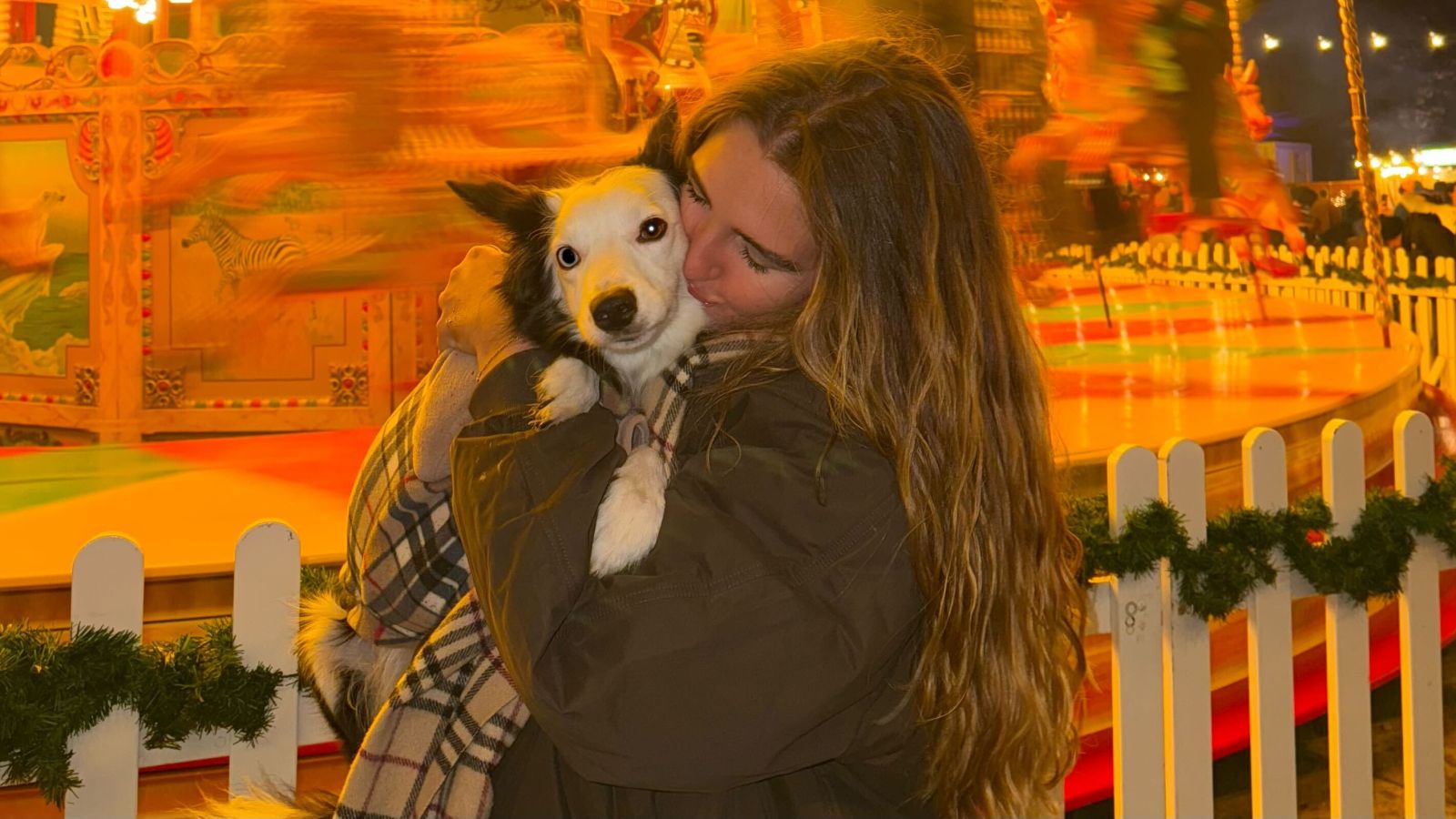 Millie with her Border Collie, Lilo, standing in front of a fairground carousel.